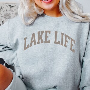以下が含まれることがあります： グレーのトレーナーに、茶色の文字で「LAKE LIFE」と書かれています。