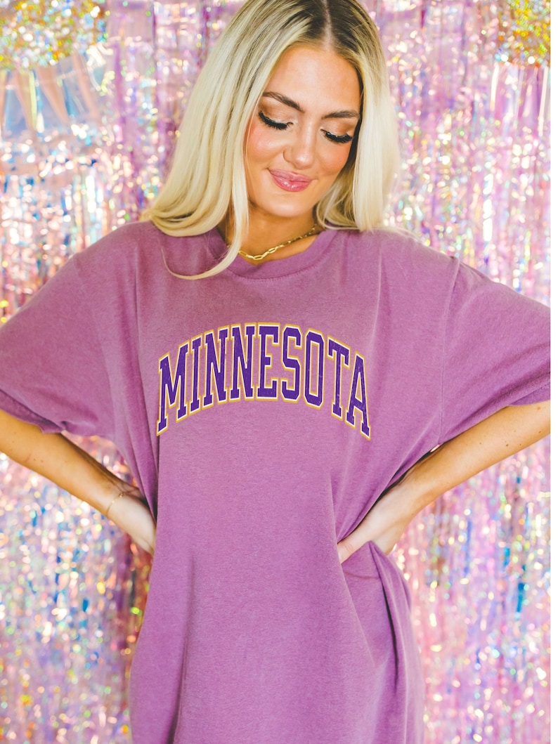 Peut inclure: Un t-shirt surdimensionn&eacute; violet avec le mot "MINNESOTA" imprim&eacute; en lettres jaunes et violettes.