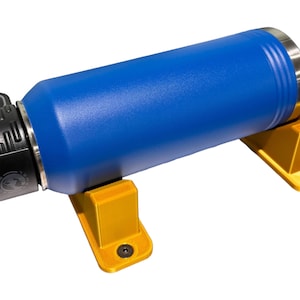 Puede incluir: Una botella de agua azul con una tapa negra y una parte superior de acero inoxidable está montada en dos soportes de plástico amarillo.