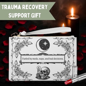 May include: White clutch bag with a black and white floral and moon design. The text "Fueled by meds, naps, and bad decisions" is displayed. The image also includes a skull, a candle, and a lipstick.