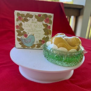 Może przedstawiać: Zestaw mydła Avon "Love Nest" z dekoracyjnym pudełkiem z motywem ptaka i kwiat&oacute;w. Zestaw zawiera mydelniczkę i trzy pachnące mydła o łącznej wadze netto 128 gram&oacute;w.
