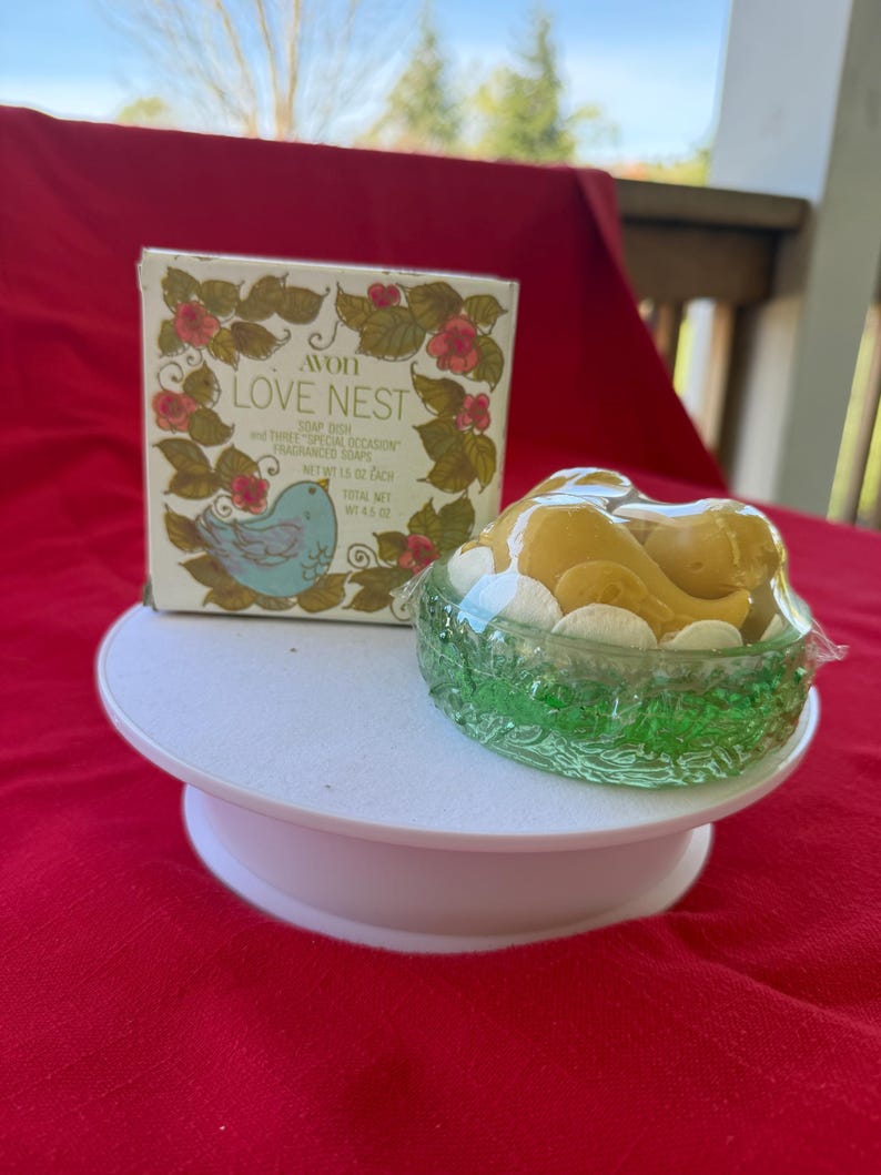 Może przedstawiać: Zestaw mydła Avon "Love Nest" z dekoracyjnym pudełkiem z motywem ptaka i kwiat&oacute;w. Zestaw zawiera mydelniczkę i trzy pachnące mydła o łącznej wadze netto 128 gram&oacute;w.