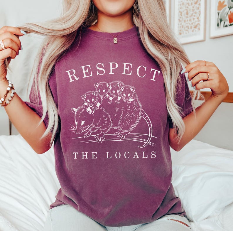 Puede incluir: Camiseta granate con un dise&ntilde;o blanco de una zarig&uuml;eya con sus cr&iacute;as y el texto "Respect The Locals". El dise&ntilde;o est&aacute; impreso en la parte delantera de la camiseta.