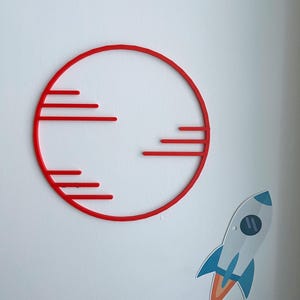 May include: A red circular wall decoration with horizontal lines, resembling a stylized sun or planet. A sticker of a rocket ship with blue and orange flames is also visible, suggesting a space or celestial theme.