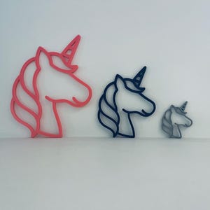 May include: Three unicorn head-shaped cookie cutters in varying sizes. The largest is pink, the medium is navy blue, and the smallest is grey. Each cutter features a horn and flowing mane.