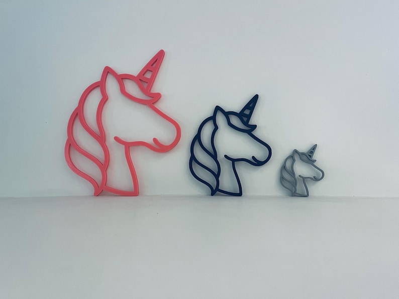 May include: Three unicorn head-shaped cookie cutters in varying sizes. The largest is pink, the medium is navy blue, and the smallest is grey. Each cutter features a horn and flowing mane.