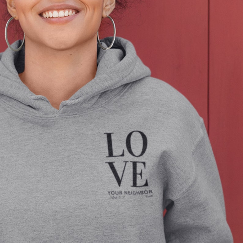 May include: A gray hooded sweatshirt with the word "LOVE" printed in black letters. Below the word "LOVE" is the text "YOUR NEIGHBOR" in smaller black letters.