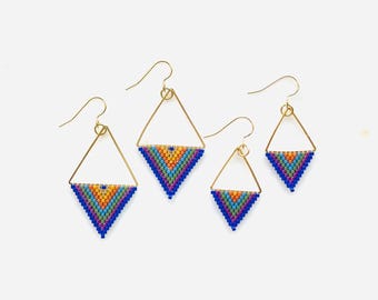 May include: A set of three pairs of triangle-shaped earrings with colorful beaded designs. The earrings are made with gold-colored wire and feature a rainbow of colors, including blue, orange, yellow, green, and purple.