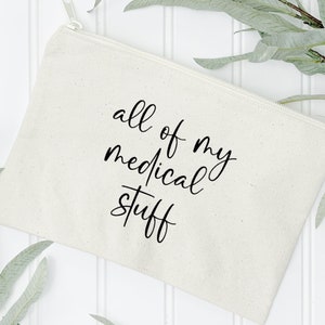 May include: A white canvas zippered pouch with black lettering that reads "all of my medical stuff".