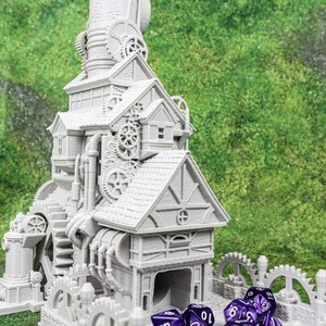May include: A detailed, gray miniature steampunk-style building with multiple levels, gears, and a water wheel. The model has a detailed facade and is set against a green, grassy background. Several purple dice are in front of the building.
