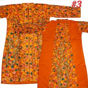 Op de afbeelding: Een oranje, lange mouwen kledingstuk met gedetailleerde bloemenborduurwerk in geel, roze en teal. Het kledingstuk heeft een paisley design en een bijpassende rug. Het nummer "#3" is zichtbaar in de rechterbovenhoek.