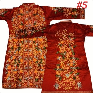 Op de afbeelding: Een bordeauxrood kledingstuk met lange mouwen en ingewikkelde bloemenborduurwerk in tinten geel, oranje, groen en wit. De borduursels bedekken de voorkant, mouwen en achterkant van het kledingstuk. Gepresenteerd op een witte achtergrond.