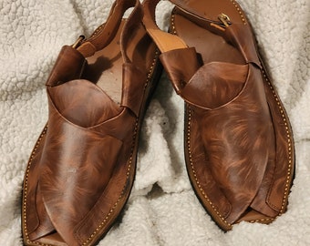 May include: A pair of brown leather sandals with a decorative stitching detail around the edges. The sandals have a closed toe and an open heel.