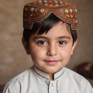 May include: A young person wearing a brown embroidered cap with a geometric pattern in red, blue, and yellow. The cap is paired with a light-colored shirt with decorative stitching around the collar.