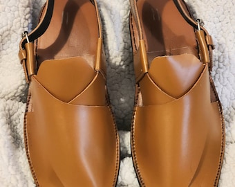 May include: A pair of brown leather sandals with a strap and buckle. The sandals have a pointed toe and a decorative stitch detail.