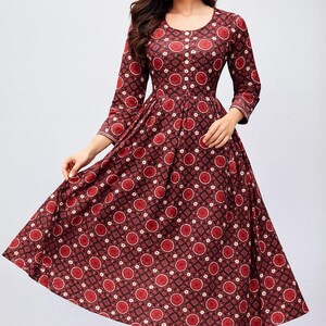 May include: A maroon dress with a geometric pattern of red circles and white accents. The dress has a round neckline, three-quarter sleeves, and a flared skirt. The model is wearing white pants.