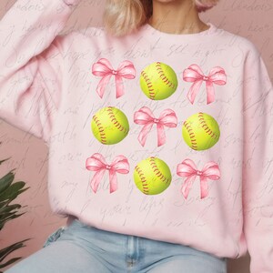May include: Pink sweatshirt with a repeating pattern of yellow softball and pink bows.
