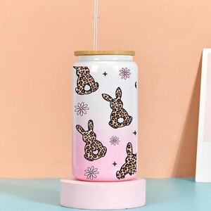 May include: White reusable water bottle with a pink ombre design and a pattern of brown and black bunnies with pink flowers. The bottle has a bamboo lid and a straw.