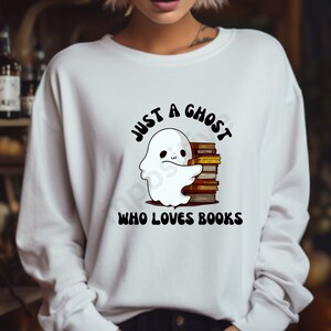 Może przedstawiać: Biała bluza z duchem trzymającym stos książek. Tekst głosi "Just a ghost who loves books."