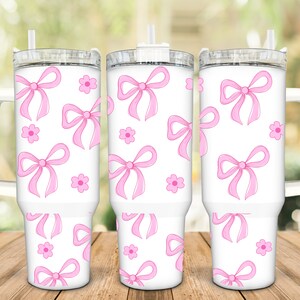 May include: Three white stainless steel tumblers with pink bows and flowers printed on them. The tumblers have lids and handles.