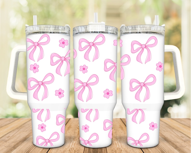 May include: Three white stainless steel tumblers with pink bows and flowers printed on them. The tumblers have lids and handles.
