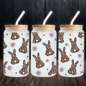 May include: Three glass tumblers with bamboo lids and straws. Each tumbler features a white background with a repeating pattern of pink flowers and brown leopard print bunnies.
