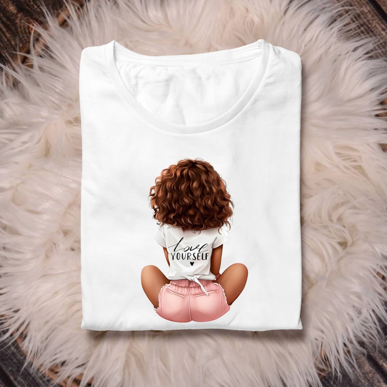 May include: White t-shirt with a graphic of a woman with brown curly hair sitting with her back to the viewer. The woman is wearing pink shorts and a white t-shirt with the text "Love Yourself" and a small heart.
