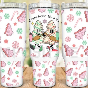 May include: White stainless steel tumbler with a handle. The tumbler features a Christmas-themed design with gingerbread cookies shaped like Christmas trees, candy canes, and snowflakes. The text on the tumbler reads "Got here lookin' like a snack".