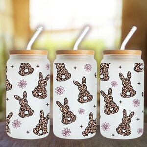 May include: Three glass tumblers with bamboo lids and clear straws. Each tumbler features a white background with a repeating pattern of pink flowers and brown bunnies with leopard print fur.