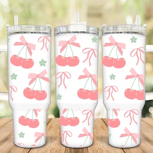 May include: Three white stainless steel tumblers with pink cherry and bow designs. The tumblers have clear lids and straws. The tumblers have handles.