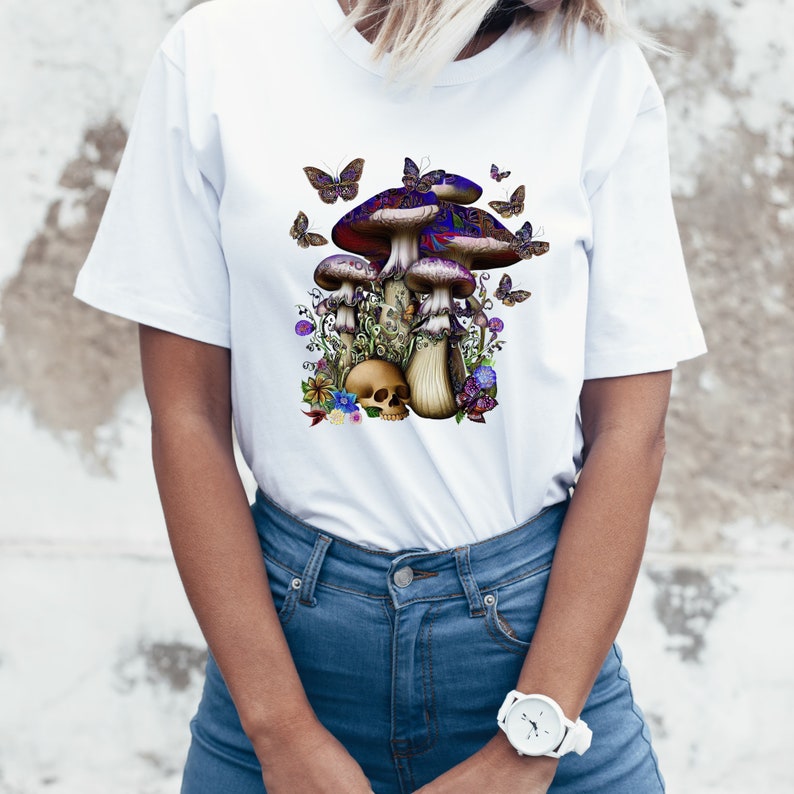 May include: White t-shirt with a graphic of three mushrooms with purple and blue caps, surrounded by butterflies and flowers. A skull sits at the base of the mushrooms.