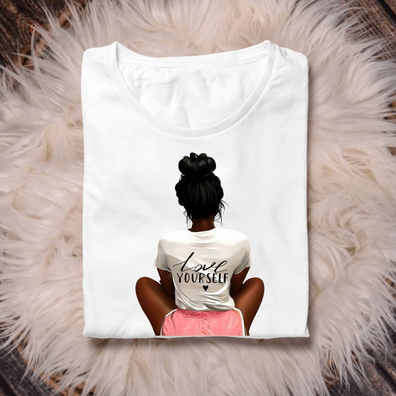 May include: White t-shirt with a black and white illustration of a woman with a bun in her hair sitting with her legs crossed. The woman is wearing pink shorts and a white t-shirt that says "love yourself" with a small black heart.