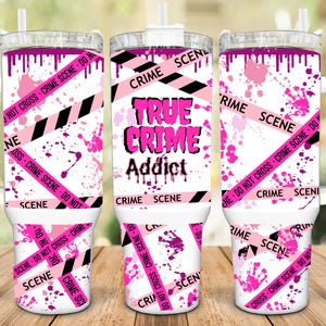 May include: A white tumbler with a pink and black crime scene tape design. The tumbler has a handle and a lid. The text "True Crime Addict" is printed on the tumbler.