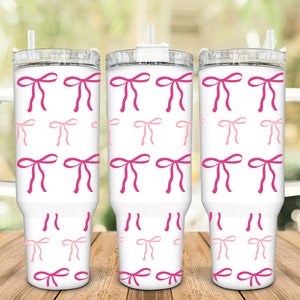 May include: Three white stainless steel tumblers with pink and light pink bows printed on the exterior. Each tumbler has a clear lid and a handle.