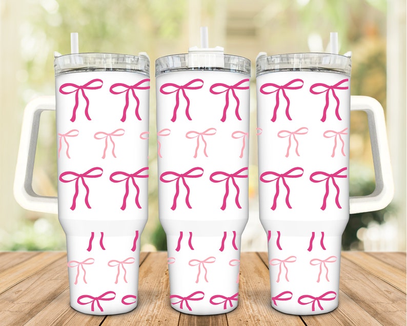May include: Three white stainless steel tumblers with pink and light pink bows printed on the exterior. Each tumbler has a clear lid and a handle.