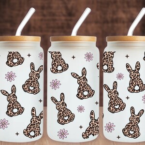 May include: Three clear glass tumblers with bamboo lids and clear straws. Each tumbler features a repeating pattern of pink flowers and brown and tan leopard print bunnies.