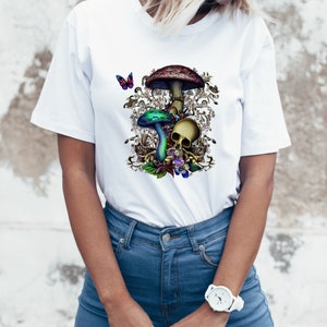 May include: White t-shirt with a colorful mushroom and skull graphic. The mushrooms are green, blue, and red with white spots. The skull is white with black eyes and a black mouth. The graphic is surrounded by a floral design.