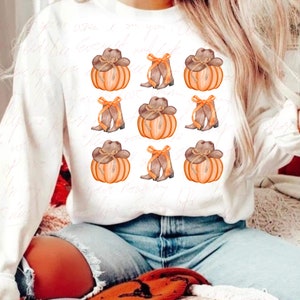 May include: White sweatshirt with a repeated pattern of orange pumpkins with brown cowboy hats and brown cowboy boots with orange bows.