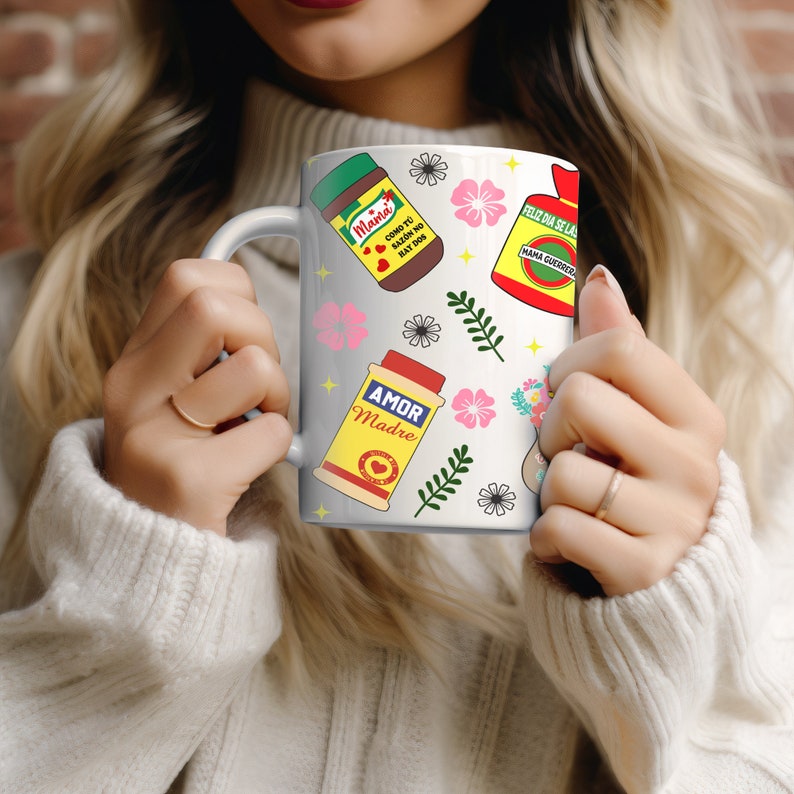 May include: White ceramic mug with a colorful design featuring various food items and the text "Mama", "Como tu saz&oacute;n no hay dos", "Amor Madre", "Feliz d&iacute;a se la Mama guerrera".