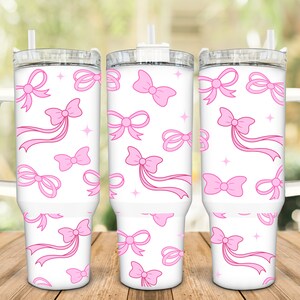 May include: Three white stainless steel tumblers with pink bows and ribbons on a white background. The tumblers have lids and handles.