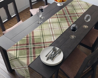 Könnte beinhalten: Ein Esstisch, der für eine Mahlzeit gedeckt ist. Der dunkle Holztisch ist mit einem karierten Tischläufer in Grün, Braun und Creme gedeckt. Weiße Teller, Besteck und Weingläser sind auf dem Tisch angeordnet. Eine Schale mit Obst steht am Kopf des Tisches.