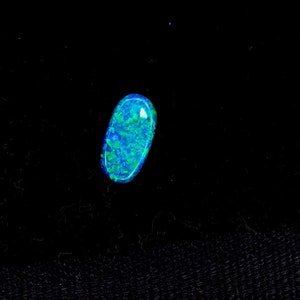 May include: A blue-green oval opal gemstone with a black background.