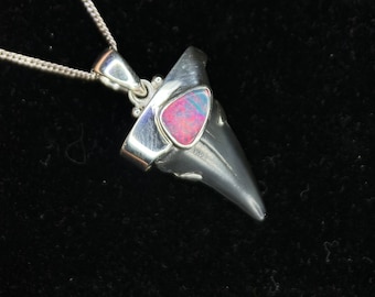 May include: A silver pendant shaped like a shark tooth with a pink opal gemstone set in the center.