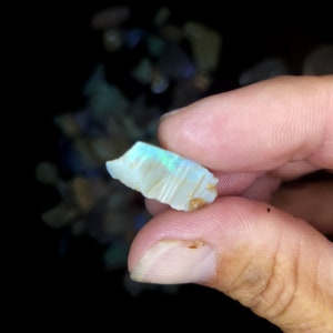 May include: A small, iridescent opal gemstone with a light blue and white colour. The opal is rough and has a natural, irregular shape.