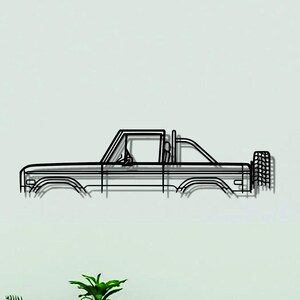 May include: A black metal wall art piece shaped as the side profile outline of a pickup truck. The design features a clear cabin structure, a truck bed, and a spare tire mounted on the rear. The lines are thin and continuous, creating a minimalist silhouette.