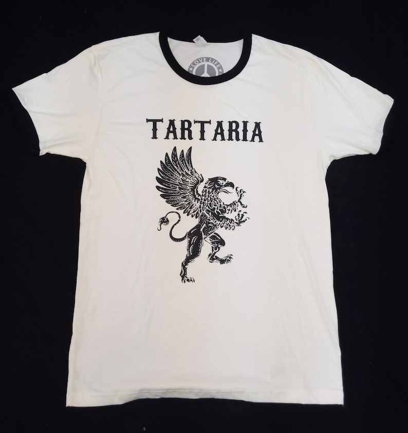May include: White t-shirt with a black ringer and a black graphic of a griffin with the word "TARTARIA" above it.