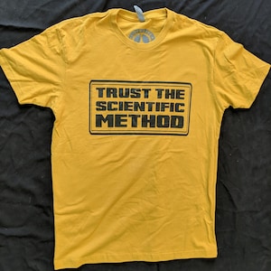 May include: A yellow t-shirt with black text that reads "TRUST THE SCIENTIFIC METHOD".
