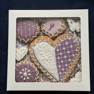 May include: A set of six heart-shaped gingerbread cookies decorated with purple and white icing. The cookies are arranged in a white box with a clear window.
