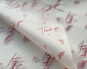 Puede incluir: Papel de seda blanco con un patrón repetido de corazones rojos y las palabras "Gracias".