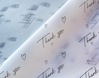 May include: White tissue paper with a repeating pattern of small hearts and the phrase "Thank you" written in cursive.